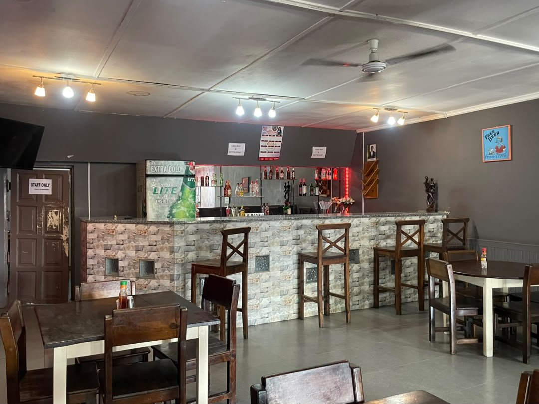 The bar with high stools, a lit bottle display and wooden dining tables