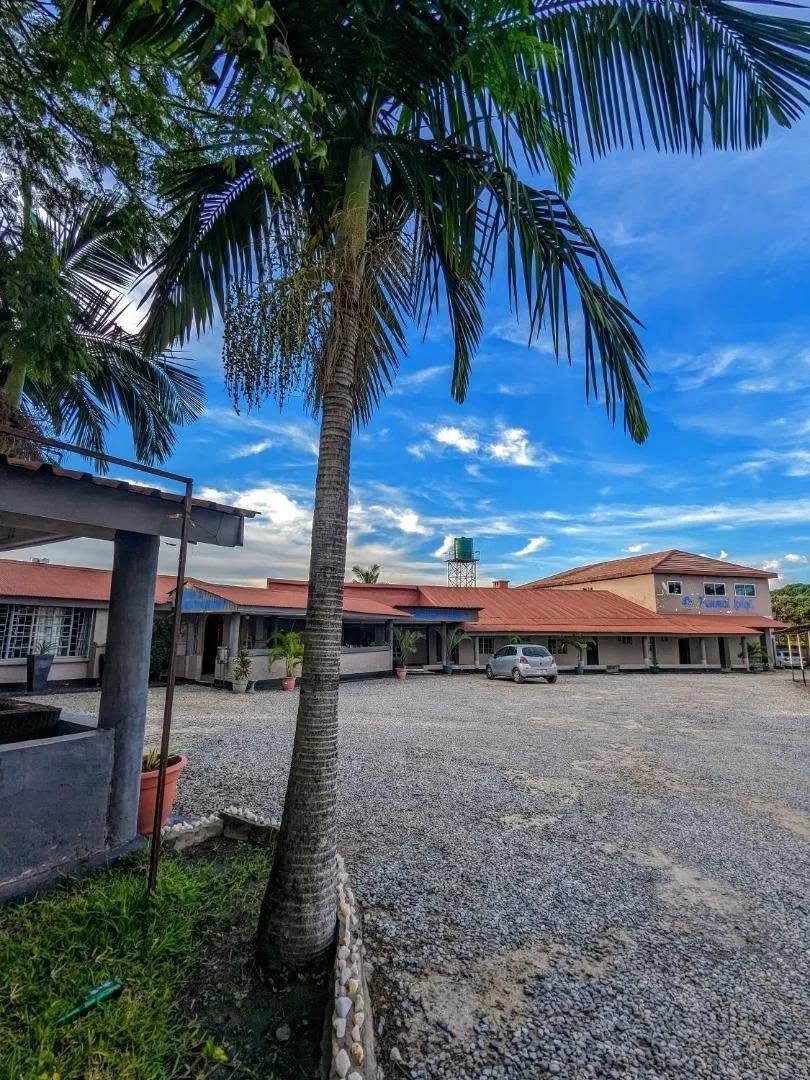 Lodge buildings with red roofs around a gravel car park, seen through palm trees under a blue sky