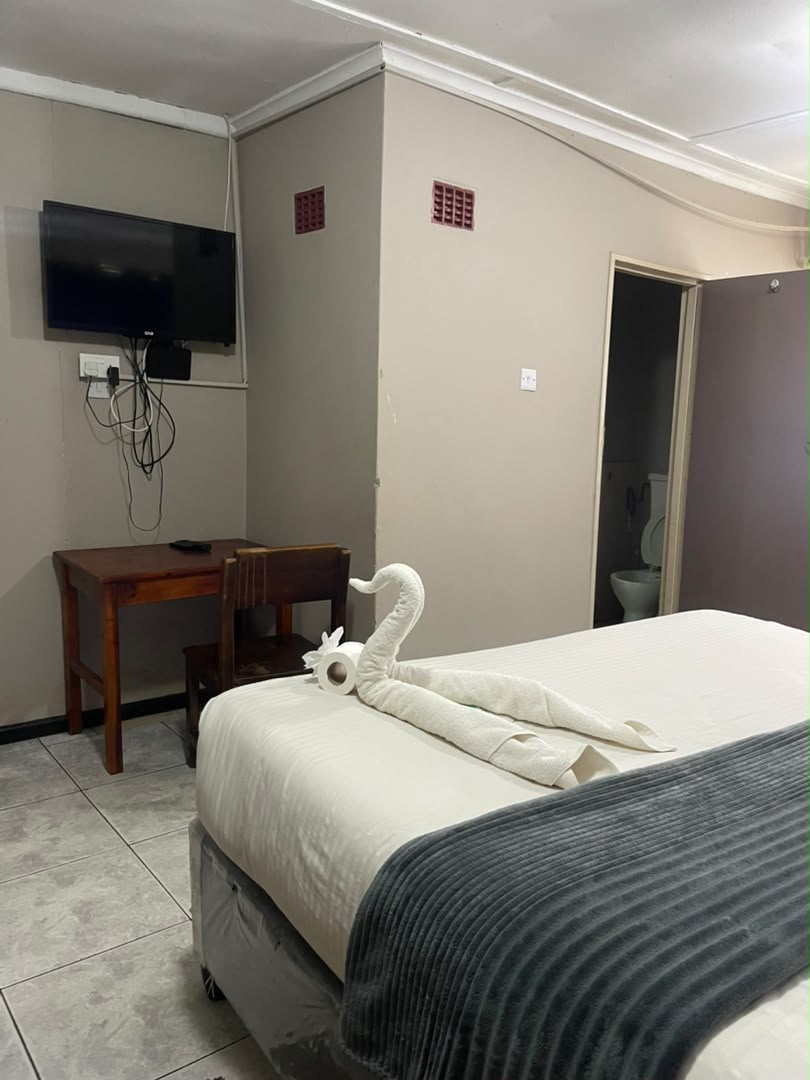 Room with a wall-mounted TV, a wooden desk and a towel swan on the bed