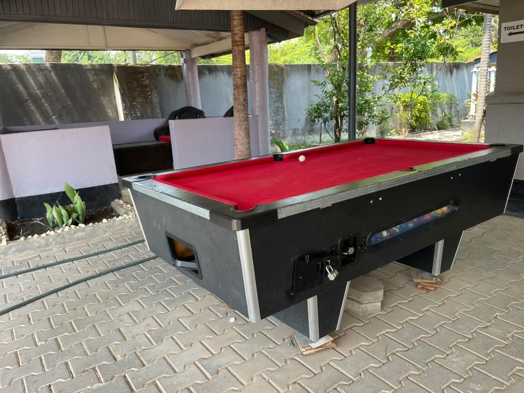 Pool table with red cloth under a covered outdoor area with garden behind