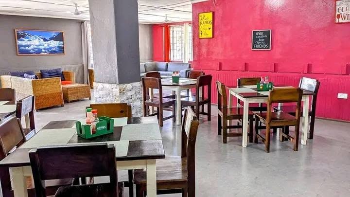 Restaurant and lounge with wooden tables, a bright pink wall and cane lounge seating