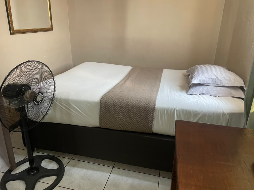 Small room with a bed, a standing fan and a wooden dresser